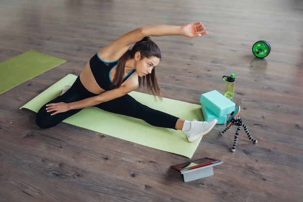 Mooie jonge vrouw die yoga beoefent, is online bezig met de leraar via een tablet. Thuis sport concept.