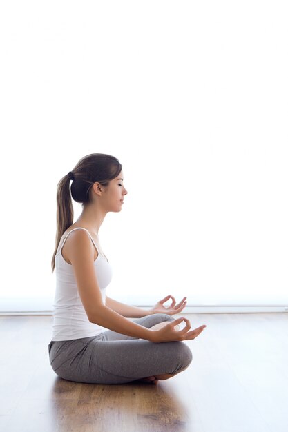 Mooie jonge vrouw doet yoga oefeningen thuis.