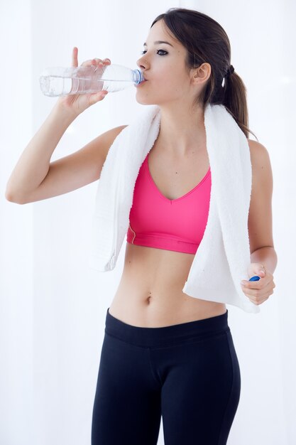 Mooie jonge vrouw drinkwater na een training thuis.