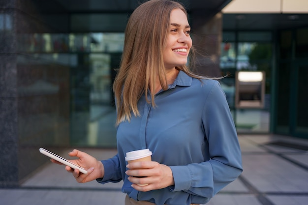 Mooie jonge vrouw gebruikt een app op haar smartphoneapparaat om een sms te sturen in de buurt van bedrijfsgebouwen