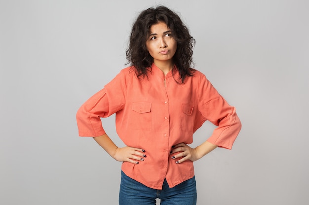 Mooie jonge vrouw gefrustreerd door een probleem, denken, verwarde emotie, geïsoleerd, oranje shirt, hipster stijl dragen