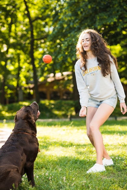 Gratis foto mooie jonge vrouw het spelen bal met haar hond in tuin