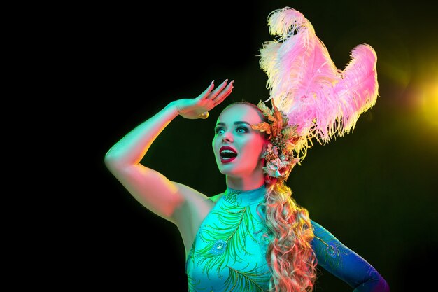 Mooie jonge vrouw in Carnaval en maskeradekostuum in kleurrijke neonlichten op zwart