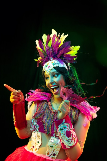 Gratis foto mooie jonge vrouw in carnavalsmasker en maskeradekostuum in kleurrijke lichten