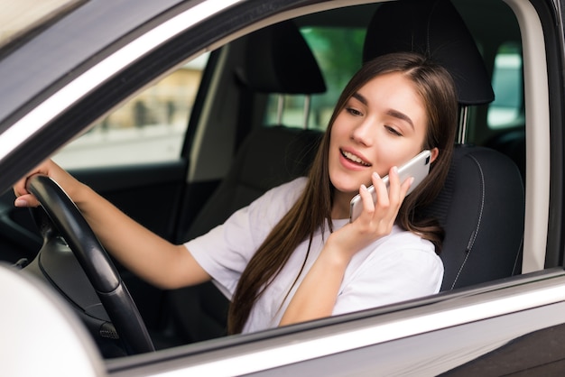 Mooie jonge vrouw in de auto zitten met laptop en praten over de telefoon.