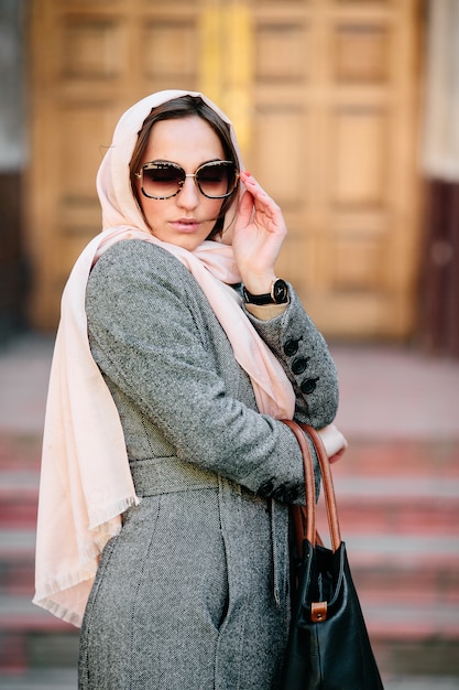 Gratis foto mooie jonge vrouw in een jas met een tas poseren