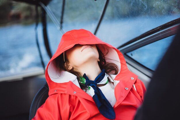 mooie jonge vrouw in een rode regenjas rijdt een prive-jacht. Stockholm, Zweden