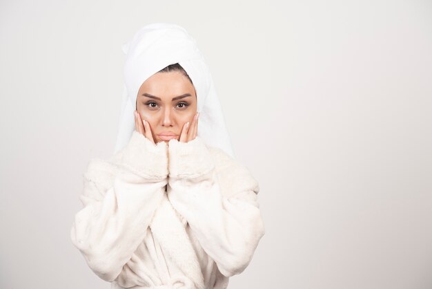 Mooie jonge vrouw in een witte badjas die zich voordeed op een witte muur.