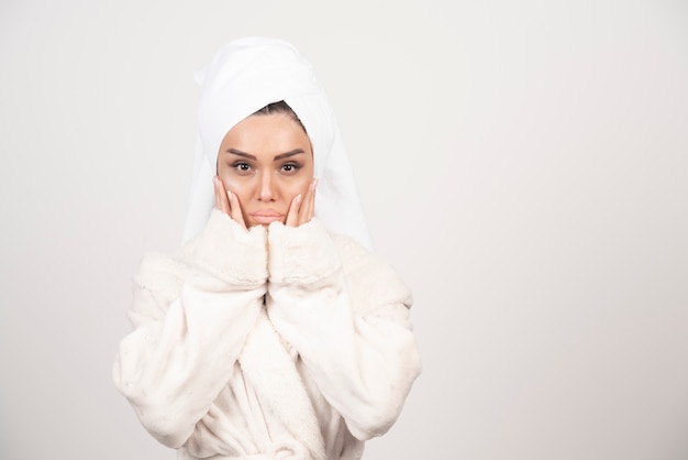 Mooie jonge vrouw in een witte badjas die zich voordeed op een witte muur