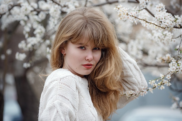 Mooie jonge vrouw in een witte trui in de kersenbloesemtuin, lentetijd Premium Foto