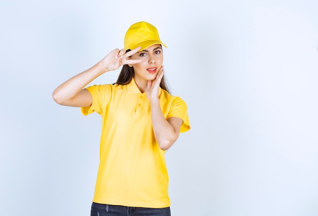 Mooie jonge vrouw in geel t-shirt en pet op zoek poseren op witte achtergrond.