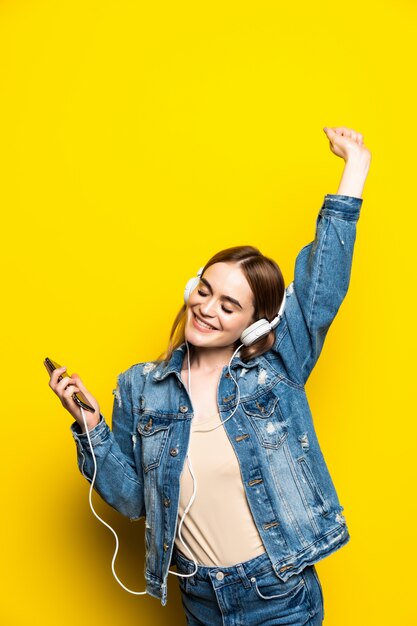 Mooie jonge vrouw in hoofdtelefoons die aan muziek luisteren en op gele muur dansen