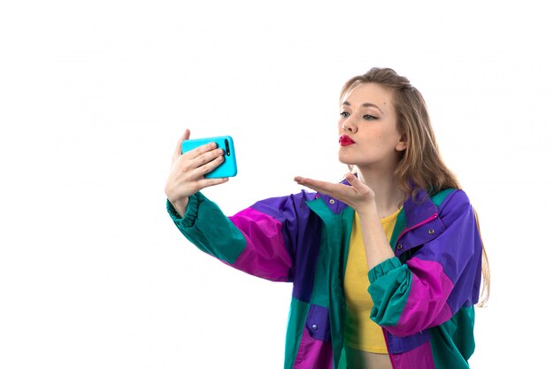 Mooie jonge vrouw in kleurrijk jasje die smartphone voor selfiefoto gebruiken