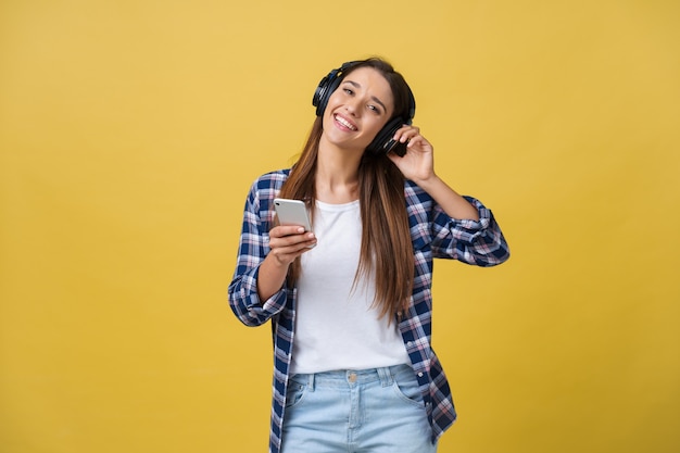 Mooie jonge vrouw in koptelefoon luisteren naar muziek en dansen op gele achtergrond.