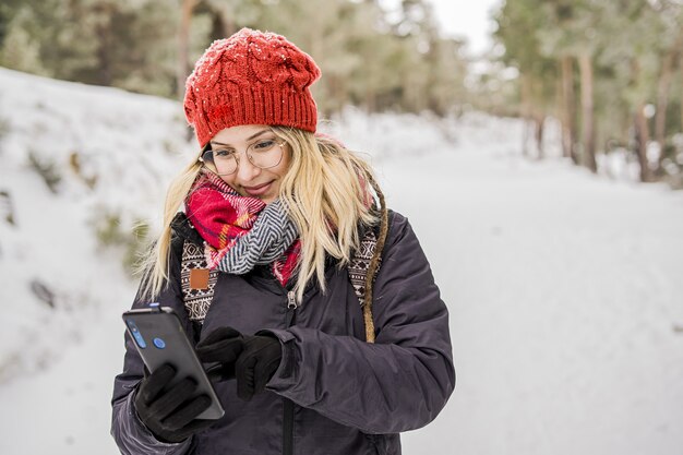 Mooie jonge vrouw in winterkleding die in het park staat bedekt met sneeuw en sms.