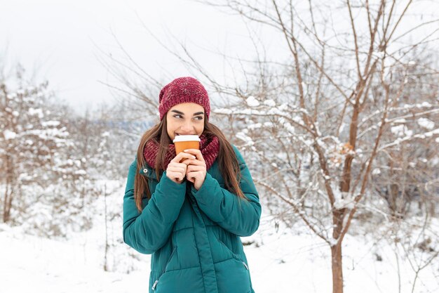 Mooie jonge vrouw in winteroutfit met wegwerpbeker gevuld met warme koffie of thee Meisje met mok warme drank in haar handen en loopt buiten in de winter