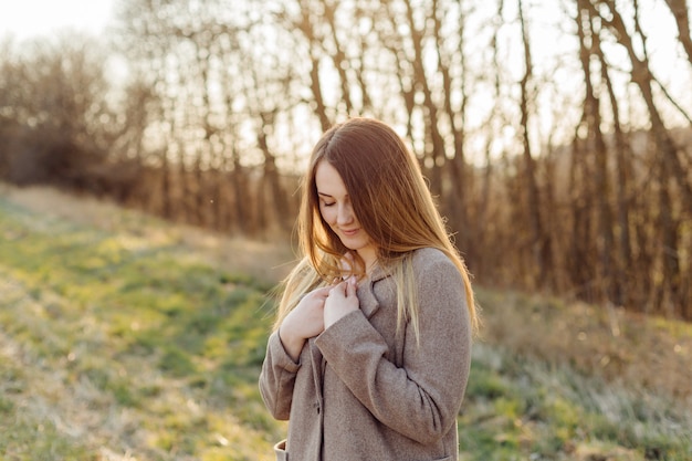 Mooie jonge vrouw in wollen jas op het bos bij zonsondergang