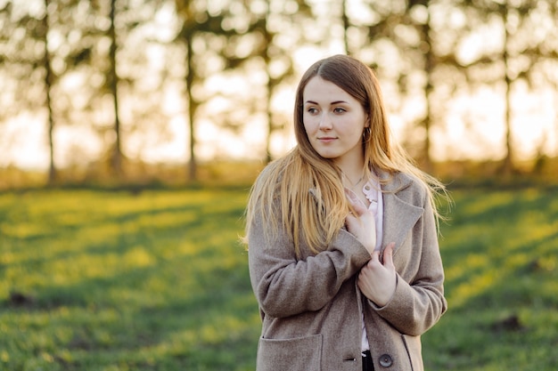 Gratis foto mooie jonge vrouw in wollen jas op het bos bij zonsondergang