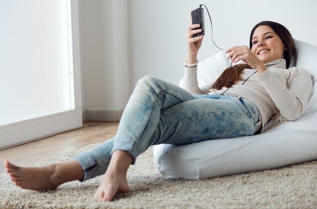 Mooie jonge vrouw luisteren naar muziek met mobiele telefoon op ho