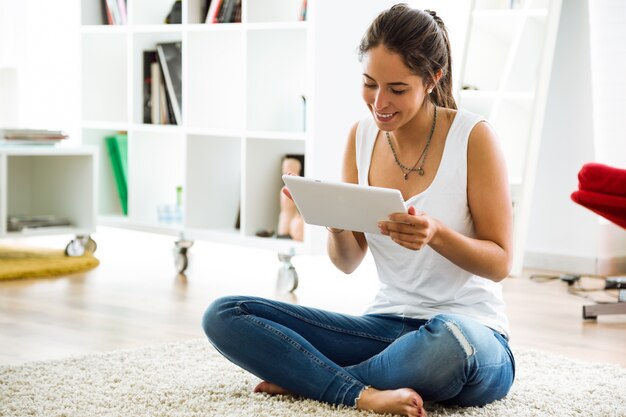 Mooie jonge vrouw met behulp van haar digitale tablet thuis.