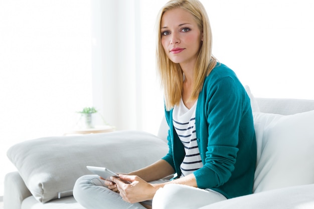 Mooie jonge vrouw met behulp van haar digitale tablet thuis.