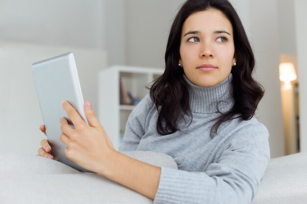 Mooie jonge vrouw met behulp van haar digitale tablet thuis.