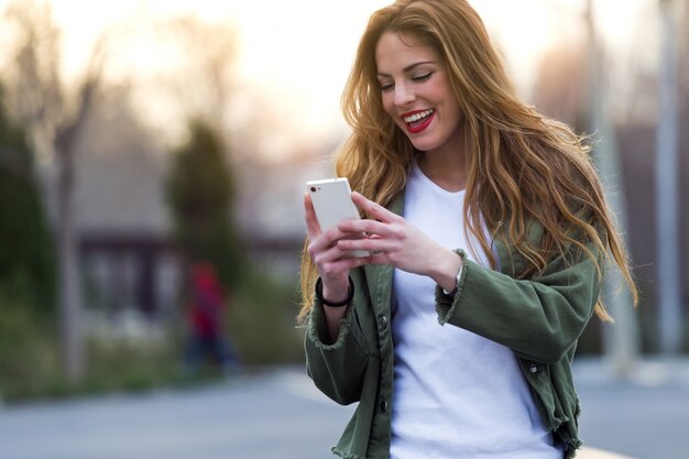 Mooie jonge vrouw met behulp van haar mobiele telefoon in de straat.