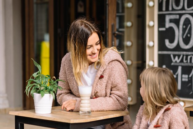 Mooie jonge vrouw met charmante dochter gekleed in warme truien zitten in cafetaria