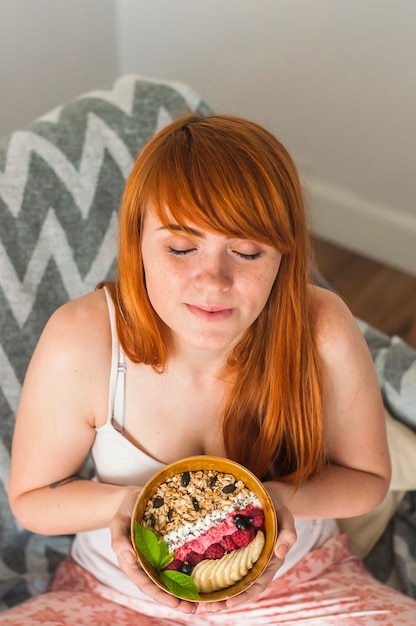 Gratis foto mooie jonge vrouw met gesloten ogen die kom havermeelgranola houden