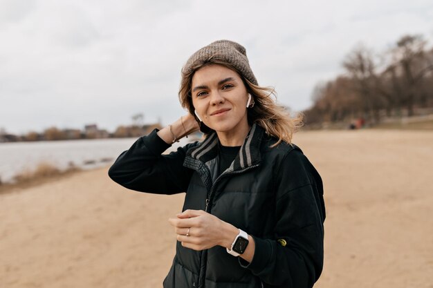 Mooie jonge vrouw met golvend kapsel poseert voor de camera met een gelukkige glimlach op het strand