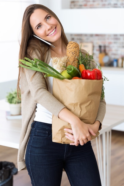 Gratis foto mooie jonge vrouw met groenten in boodschappentas thuis.