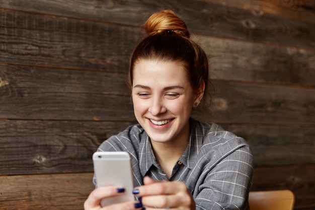 Gratis foto mooie jonge vrouw met haarknotje met generieke slimme telefoon, nieuwsfeed op sociale media controleren