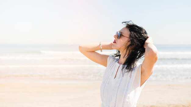 Mooie jonge vrouw met hand op haar hoofd staande in de buurt van de zee op het strand