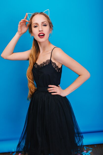 Mooie jonge vrouw met lang blond haar op feestje, poseren. Het dragen van een prachtige zwarte jurk, diadeem met kattenoren in diamanten op het hoofd.