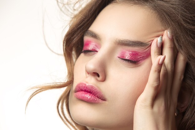 Mooie jonge vrouw met lang golvend zijdeachtig haar, natuurlijke make-up met hand in de buurt van kin geïsoleerd op een witte muur. Model met natuurlijke make-up.