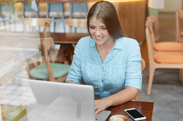 Mooie jonge vrouw met lang haar zittend in café met laptop
