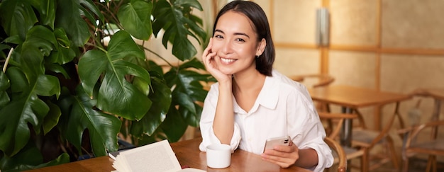 Mooie jonge vrouw met smartphone koffie drinken in café en glimlachend ontspannen met favoriet