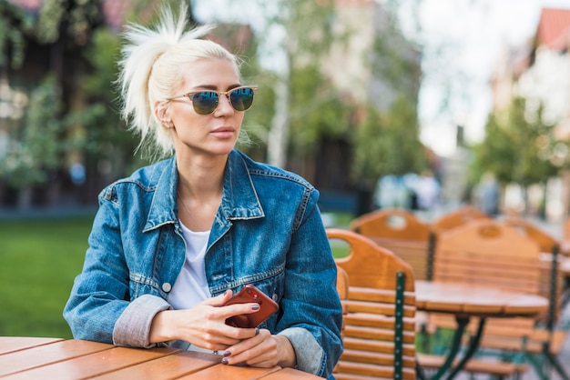 Mooie jonge vrouw met smartphone zit in openlucht café