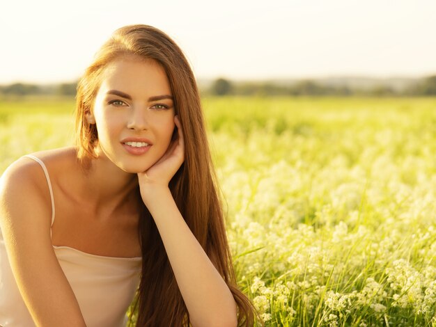 Mooie jonge vrouw op aard over de achtergrond van een veld zomer.