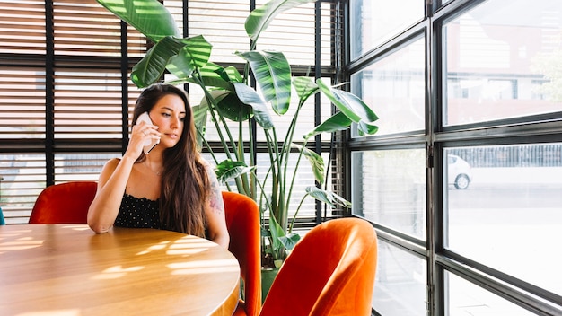 Mooie jonge vrouw zitten in restaurant praten op mobiele telefoon