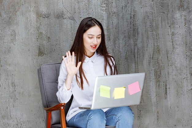 Mooie jonge vrouw zittend op fauteuil bellen met laptop. Hoge kwaliteit foto