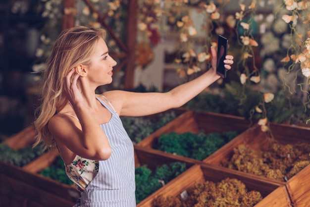 Mooie jonge vrouwelijke bloemist die selfie op mobiele telefoon in de winkel nemen