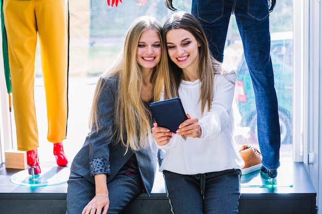 Mooie jonge vrouwen die digitale tablet in de klerenopslag bekijken