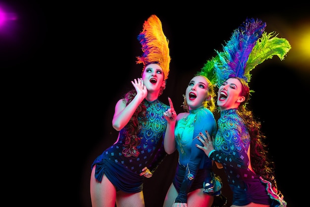 Mooie jonge vrouwen in Carnaval, stijlvol maskeradekostuum met veren op zwarte muur in neonlicht