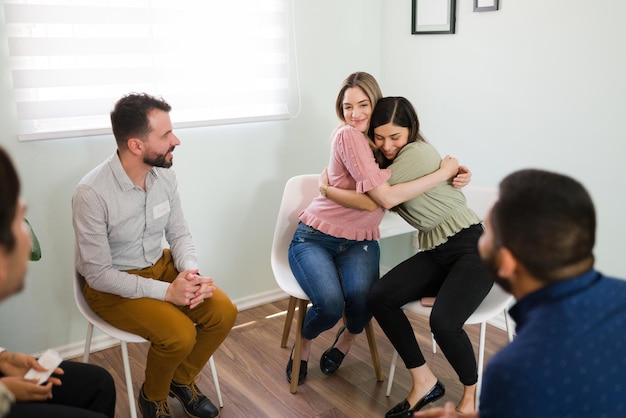 Mooie jonge vrouwen knuffelen en glimlachen na het beëindigen van een groepstherapiesessie. Ik voel me gelukkig om samen mijn geestelijke gezondheidsproblemen te overwinnen