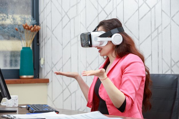 Mooie jonge zakenvrouw die een VR-bril draagt en haar hand in de lucht opent Foto van hoge kwaliteit