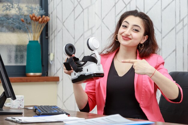 Mooie jonge zakenvrouw die een VR-bril vasthoudt en er met de vinger op wijst Hoge kwaliteit foto