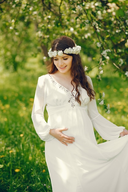 Mooie jonge zwangere meisje in een lange witte jurk en een krans op haar hoofd