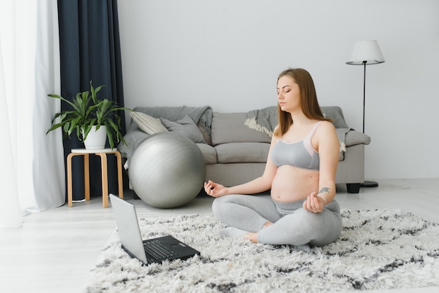 Mooie jonge zwangere vrouw met laptop die thuis traint