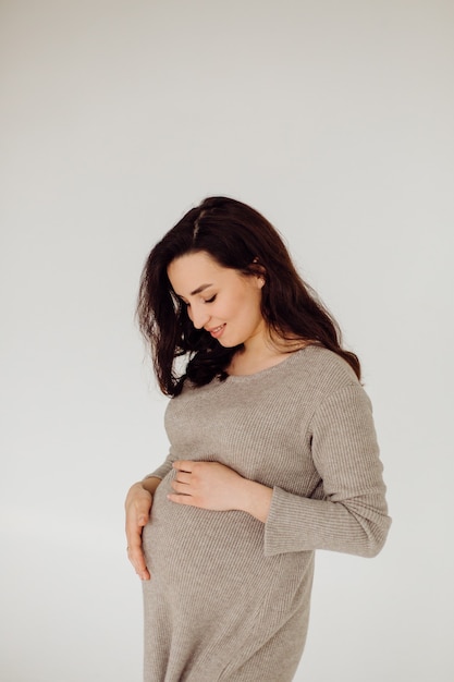 Mooie jonge zwangere vrouw poseren in studio in jurk
